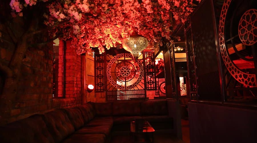Cherry blossom tree overhanging a red-lit seating area with ornate wall panels inside Junoon Cafe